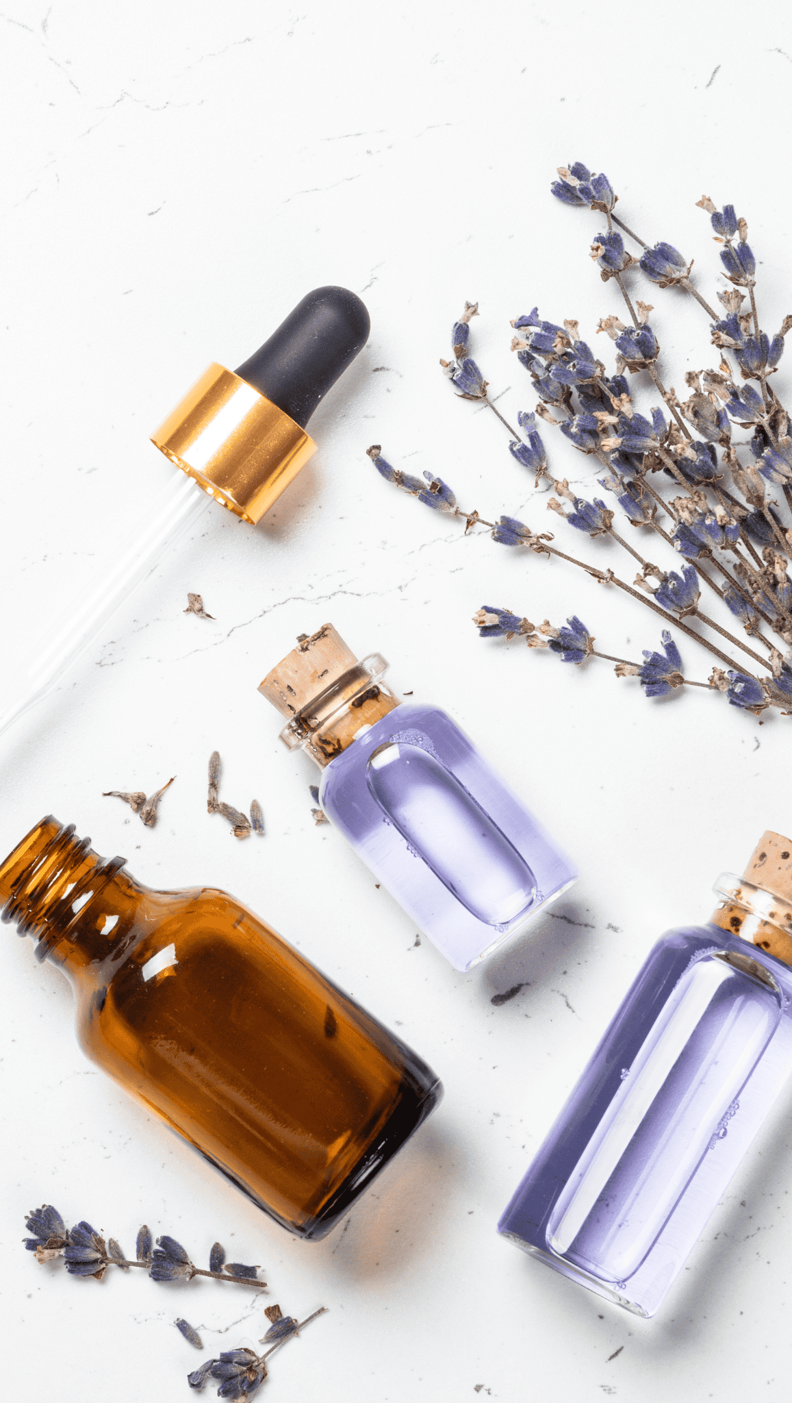 Three glass bottles—one amber and two clear with purple liquid—lie on a white surface alongside a dropper and dried lavender sprigs, perfect for enhancing your Night Shower Routine.
