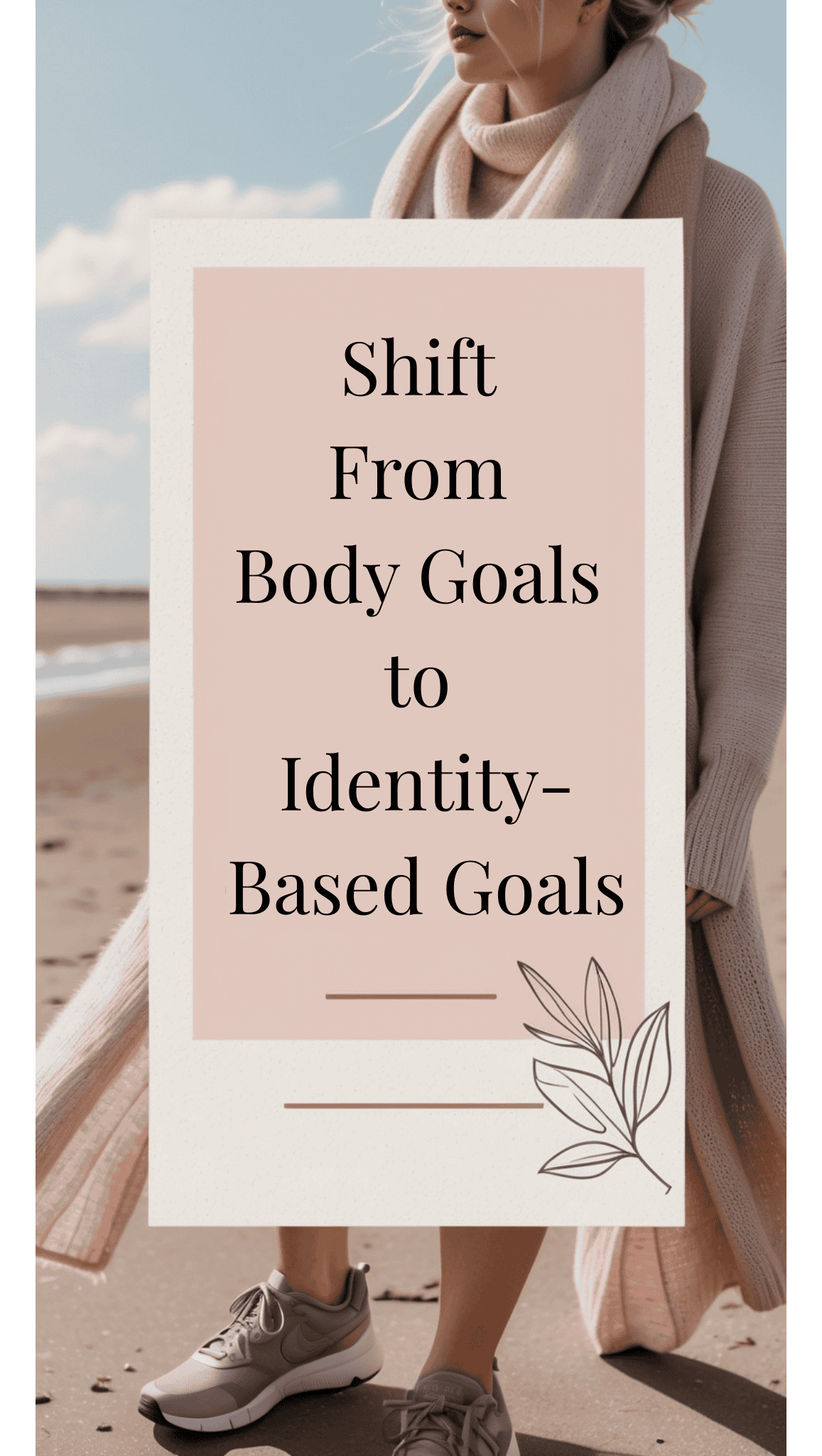 A woman in a long beige cardigan and sneakers stands on a beach holding a sign that reads, Shift From Fitness Goals to Identity-Based Goals, embracing powerful Mindset Shifts.