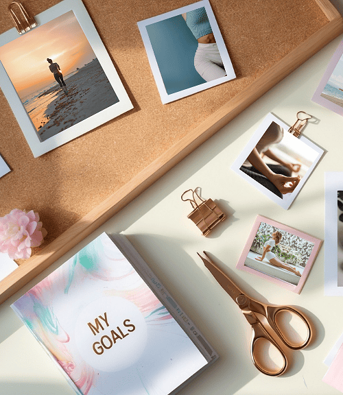 A flat lay of a desk with goal-setting items: photos, a “My Goals” notebook, scissors, binder clips, sticky notes, green tea, succulents, and healthy food images—perfect for Fit Body Vision Board Ideas.